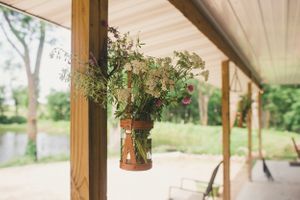 Rustic hanging floral arrangement in mason jar on wooden porch post.
