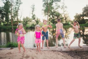 Children playing and splashing at the edge of a lake during sunset.