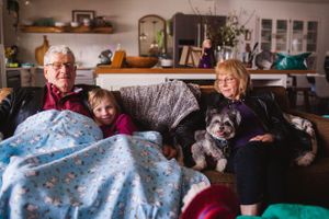 A cozy scene of people relaxing on a sofa with a small dog under a blue blanket in a home setting.