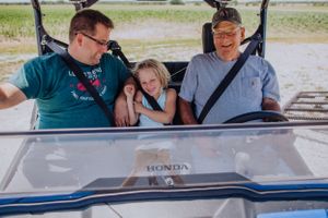 Three people seated in a Honda golf cart or utility vehicle outdoors.