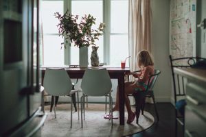 A dining room scene with mint green chairs and a person seated at a wooden table near a window.