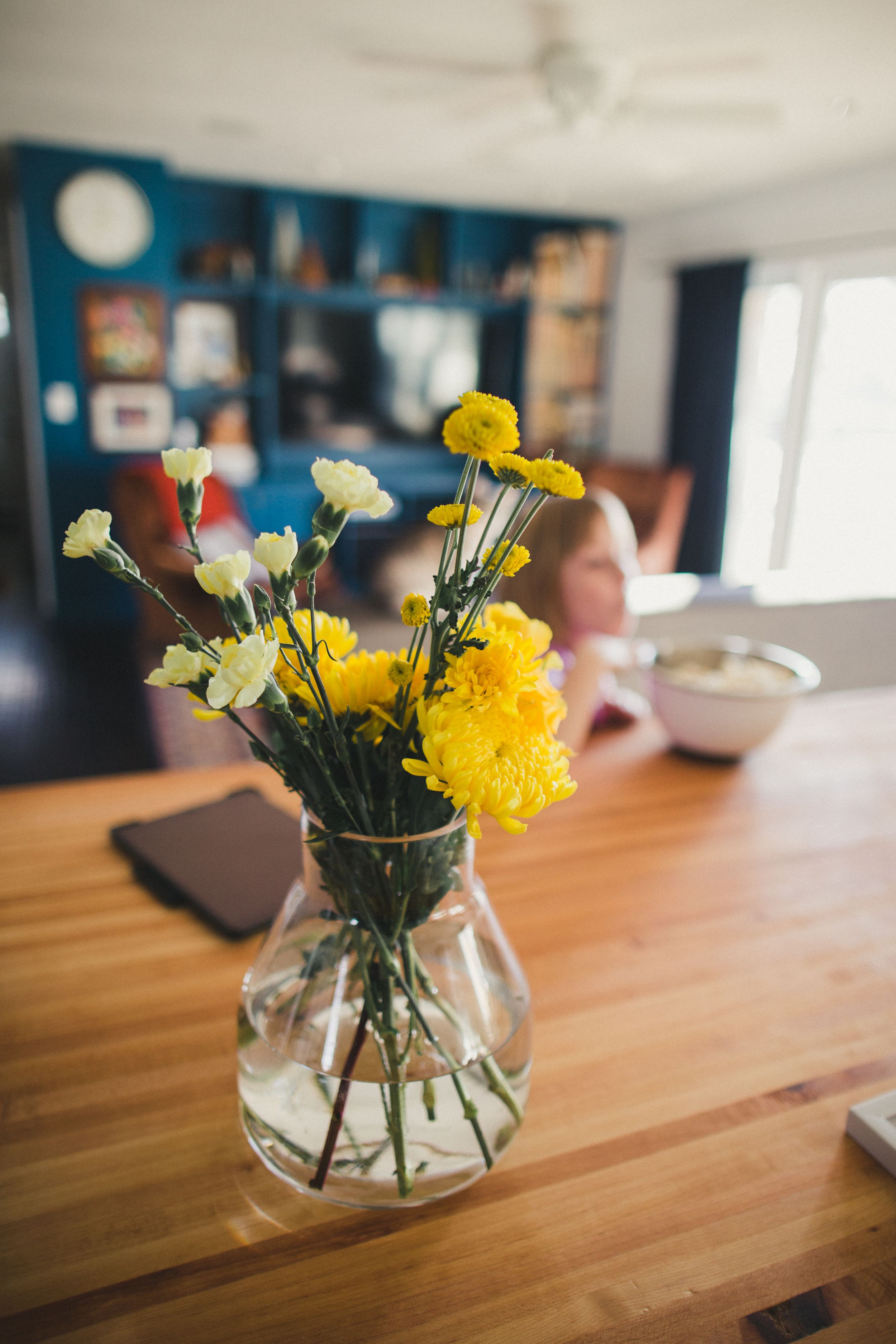 Yellow and white flowers arranged in a clear glass vase on a wooden table surface.