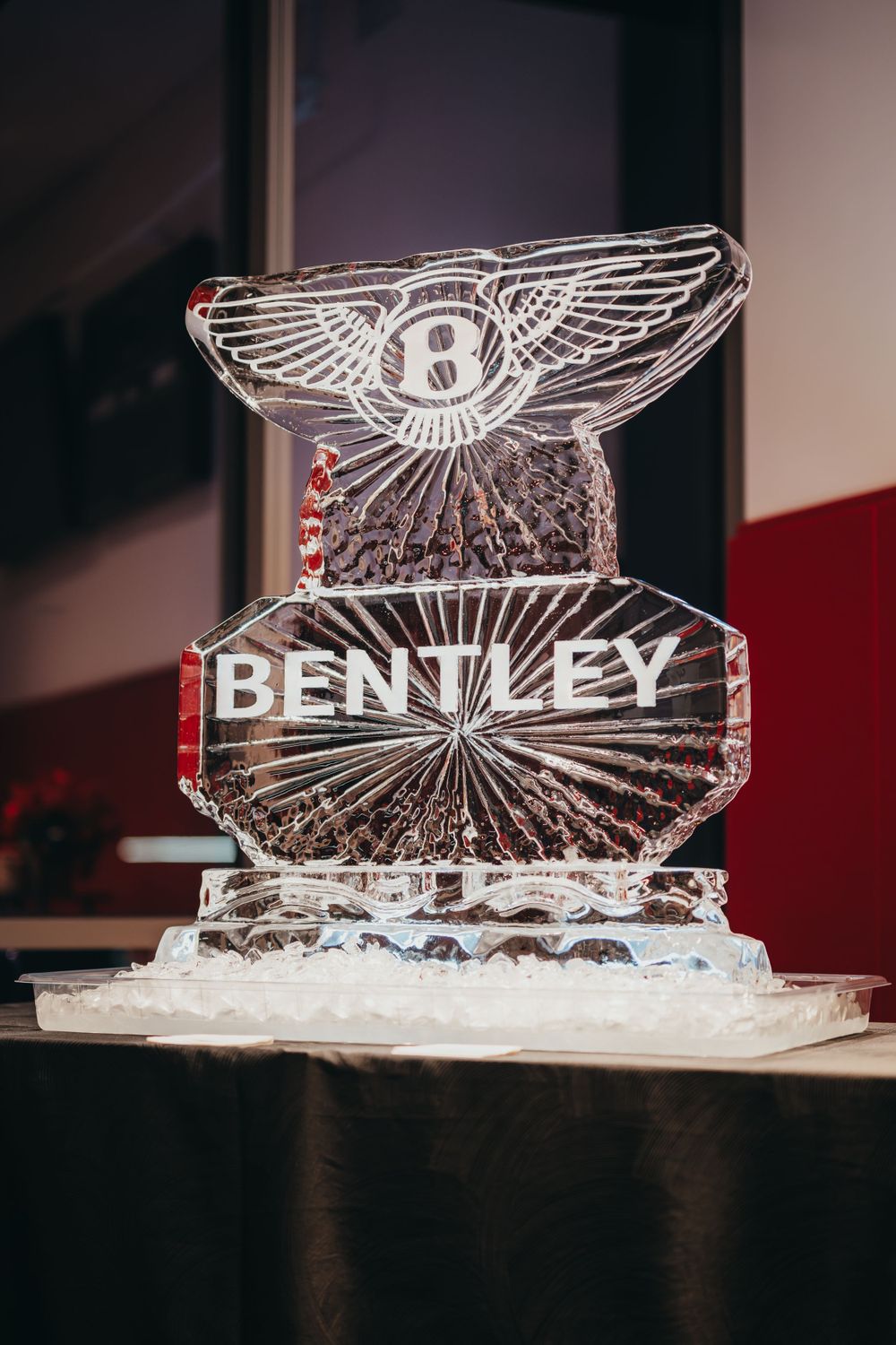 Ice sculpture displaying Bentley logo and wings illuminated on dark surface.