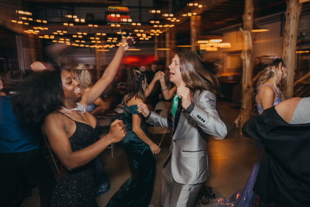 People dancing and celebrating at a nighttime party under string lights.