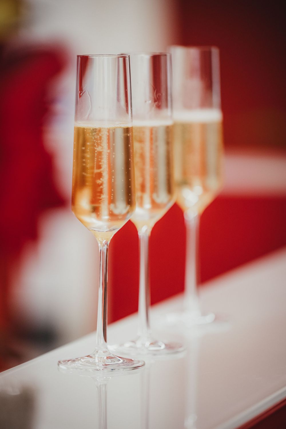 Row of champagne flutes filled with sparkling wine on white counter with red ambient lighting.
