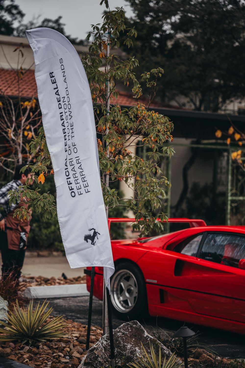 Red Ferrari sports car parked with Ferrari branded flags in outdoor setting.