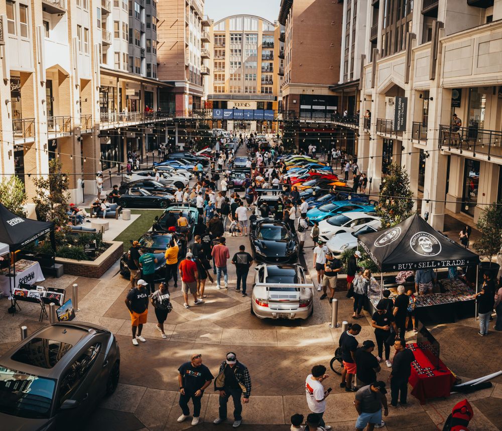 Urban street scene with parked cars and pedestrians walking along storefronts.