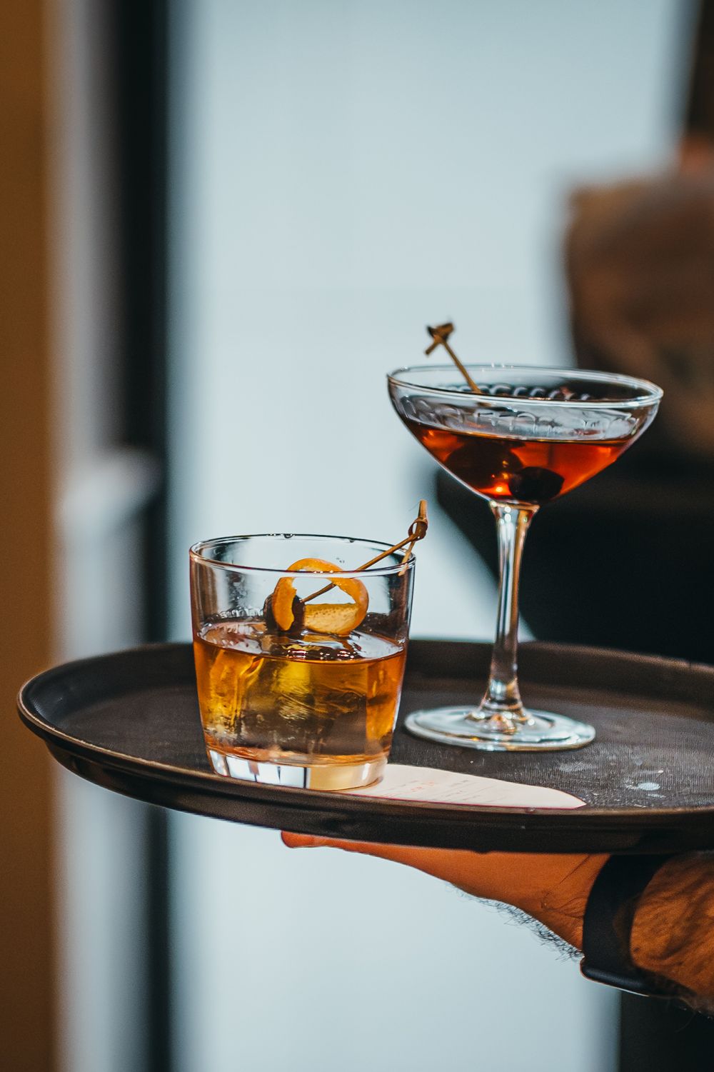 Elegant cocktails served on wooden tray with garnishes in upscale setting.