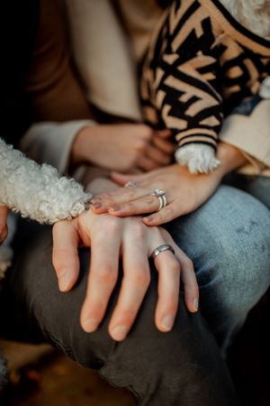 Close-up of engagement rings with a furry paw touching hands on denim jeans.