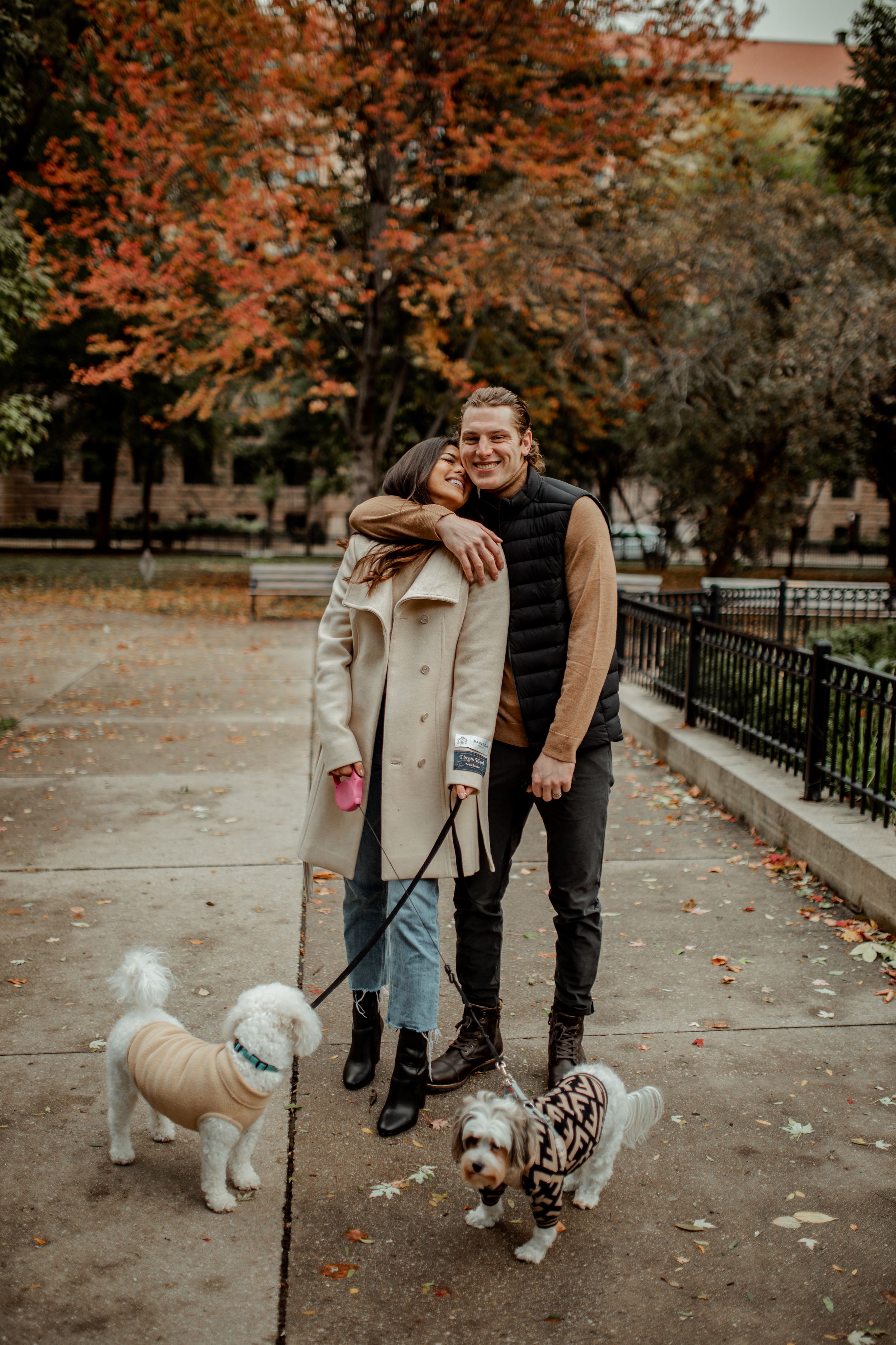 A couple poses with their two dogs on a path surrounded by fall foliage.