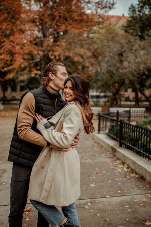 A romantic embrace between a couple on an autumn day with orange trees in the background.