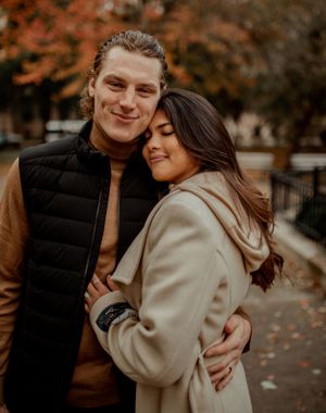 A couple shares an intimate close-up moment among fall foliage in an urban park setting.