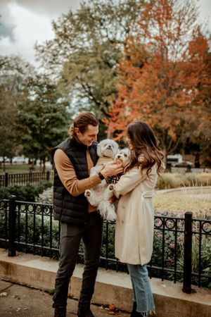 A couple plays with their small white dogs during an autumn photoshoot in the park.