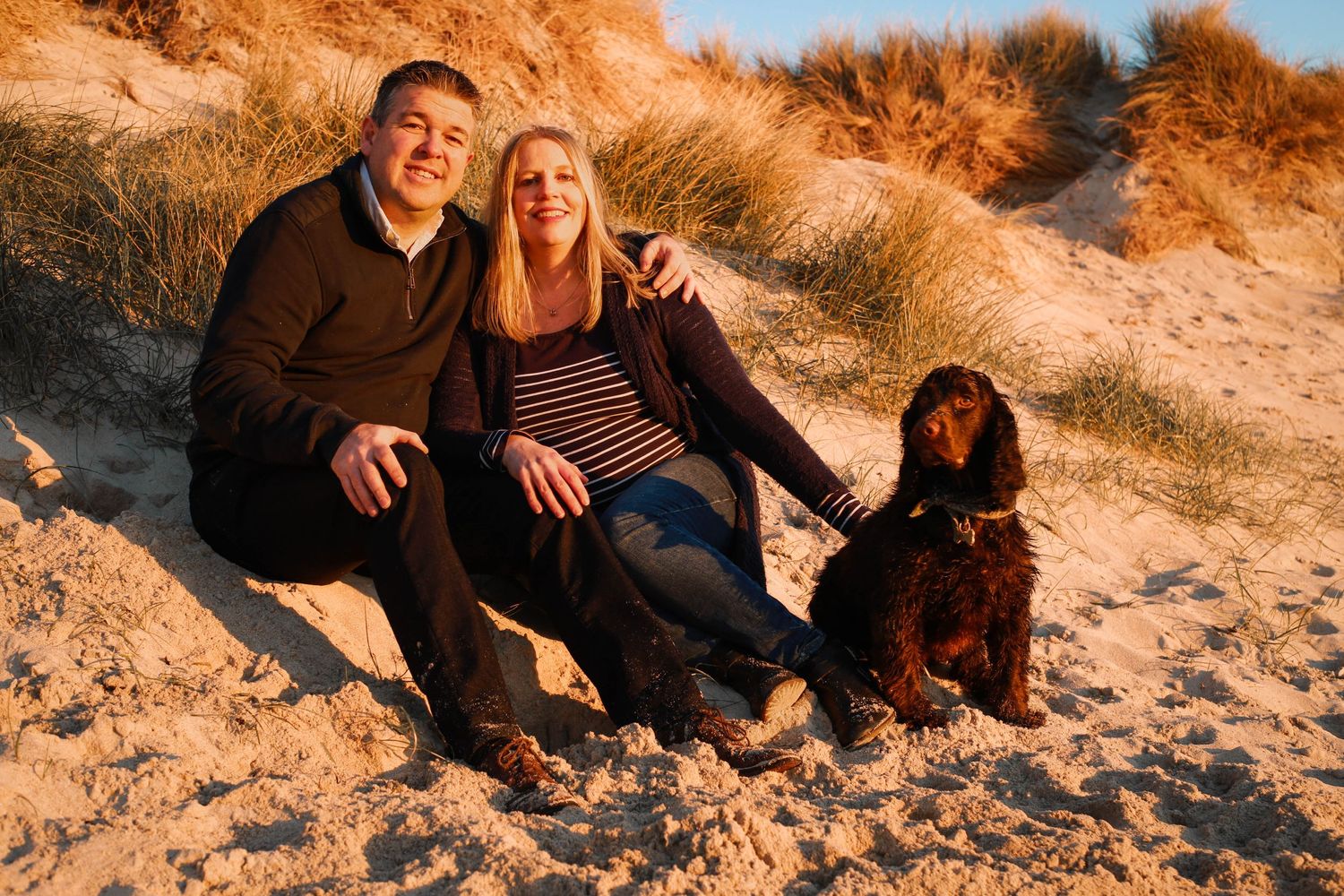 Couple with dog enjoying sunset at sandy beach dunes.
