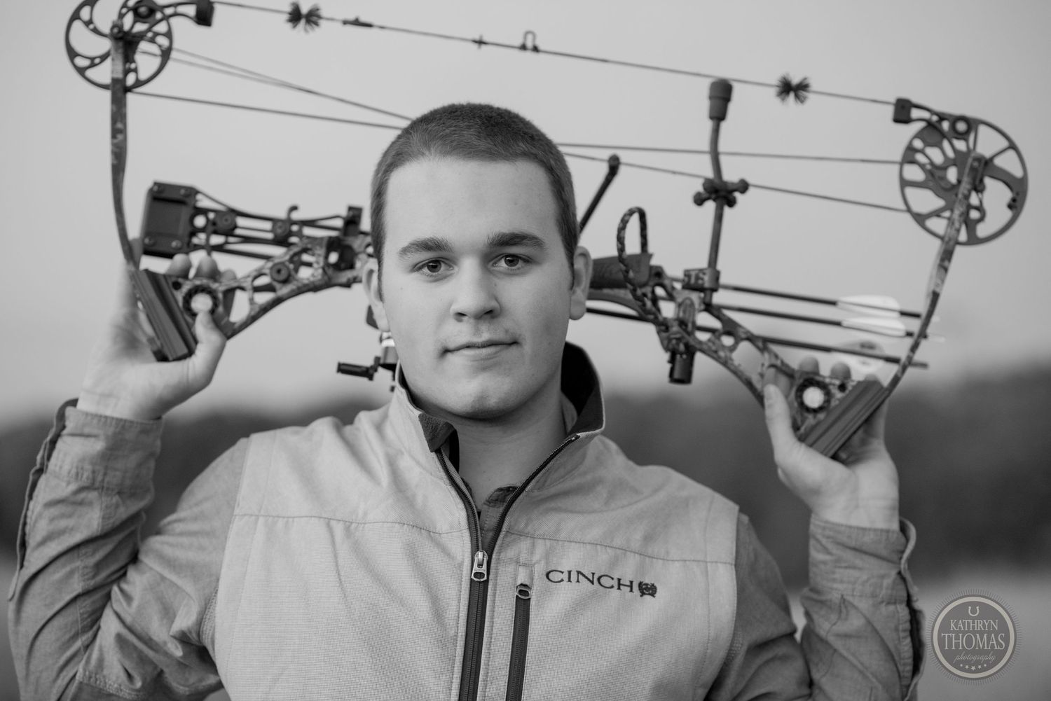 Black and white portrait of archer holding compound bow overhead.