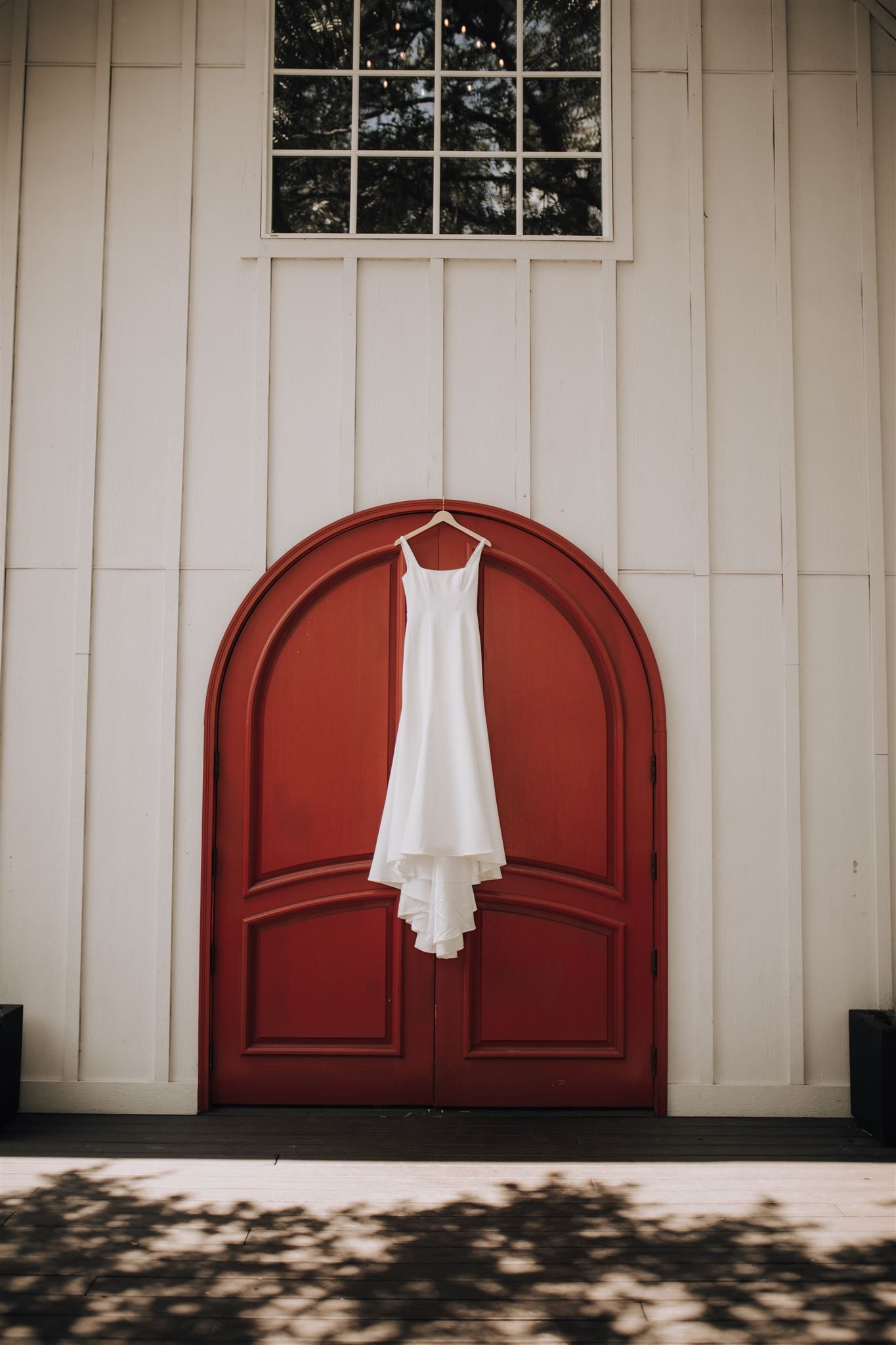 dress hung in front of grand red doors of chapel at Carriage House wedding venue