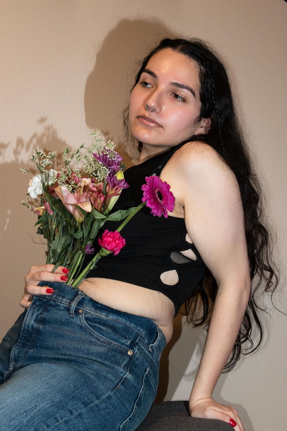 Casual portrait holding colorful flower bouquet against neutral wall.