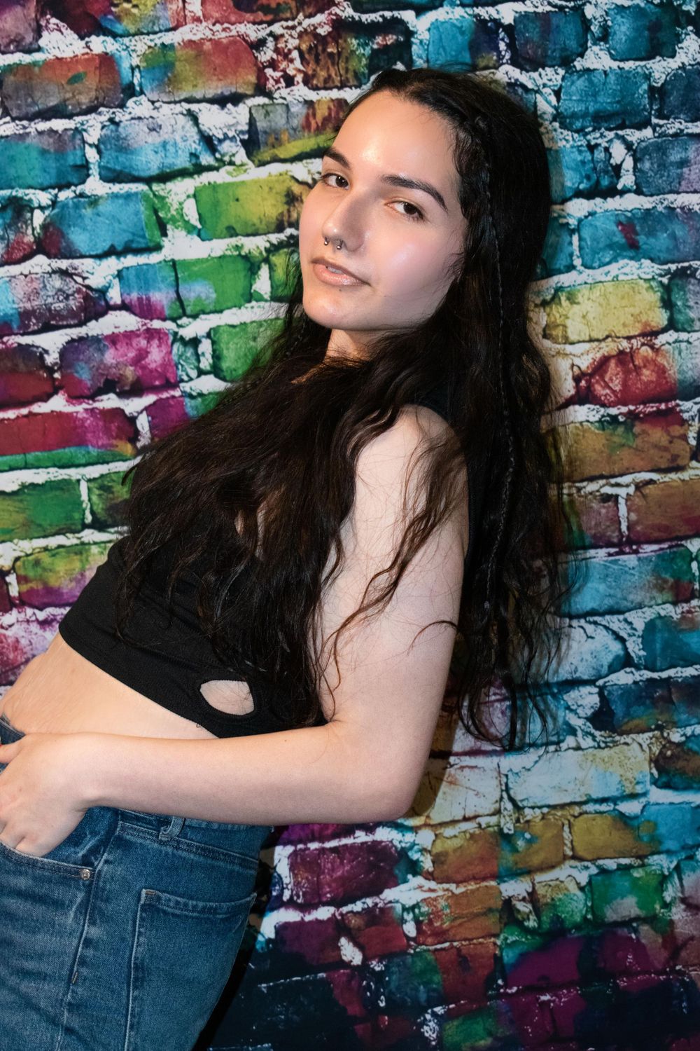Portrait against colorful graffiti wall with person in black crop top and jeans.