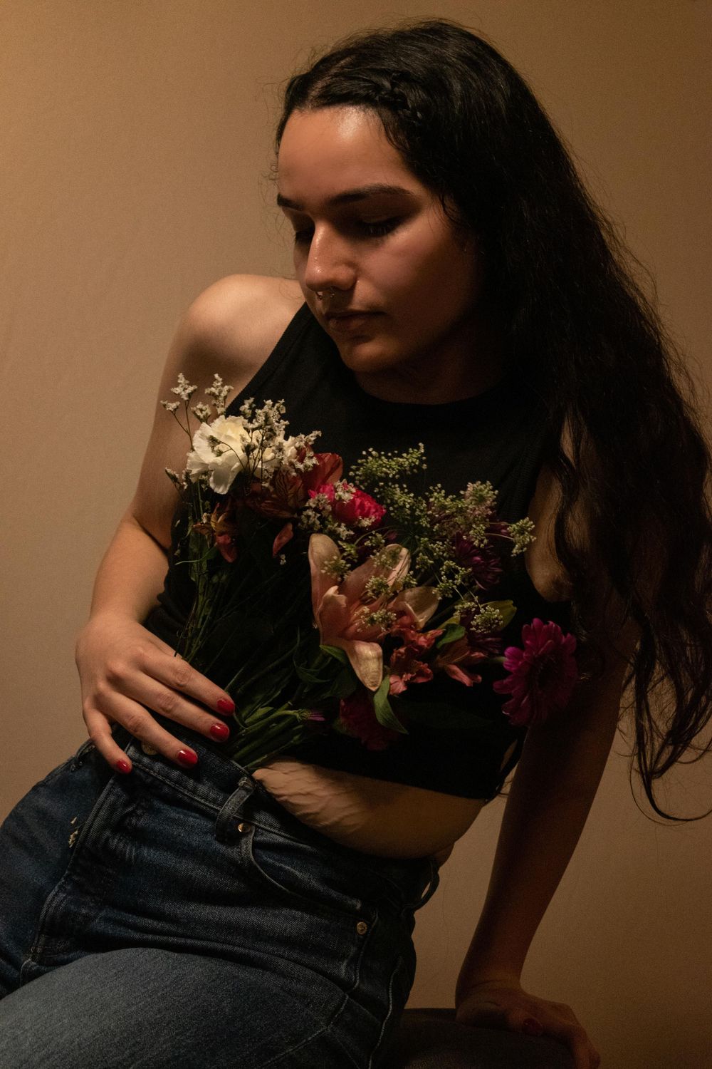 Artistic portrait featuring dark-haired figure in black top holding colorful floral bouquet against warm brown background.