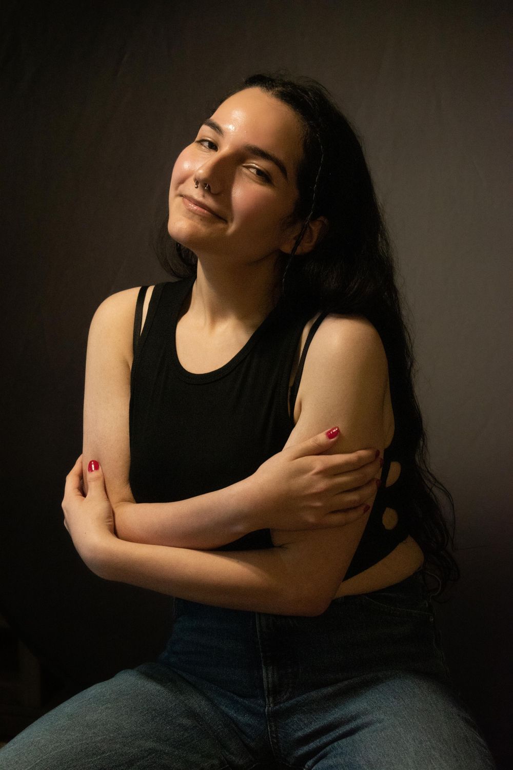 Portrait of person in black tank top with crossed arms and long dark hair in dramatic lighting.