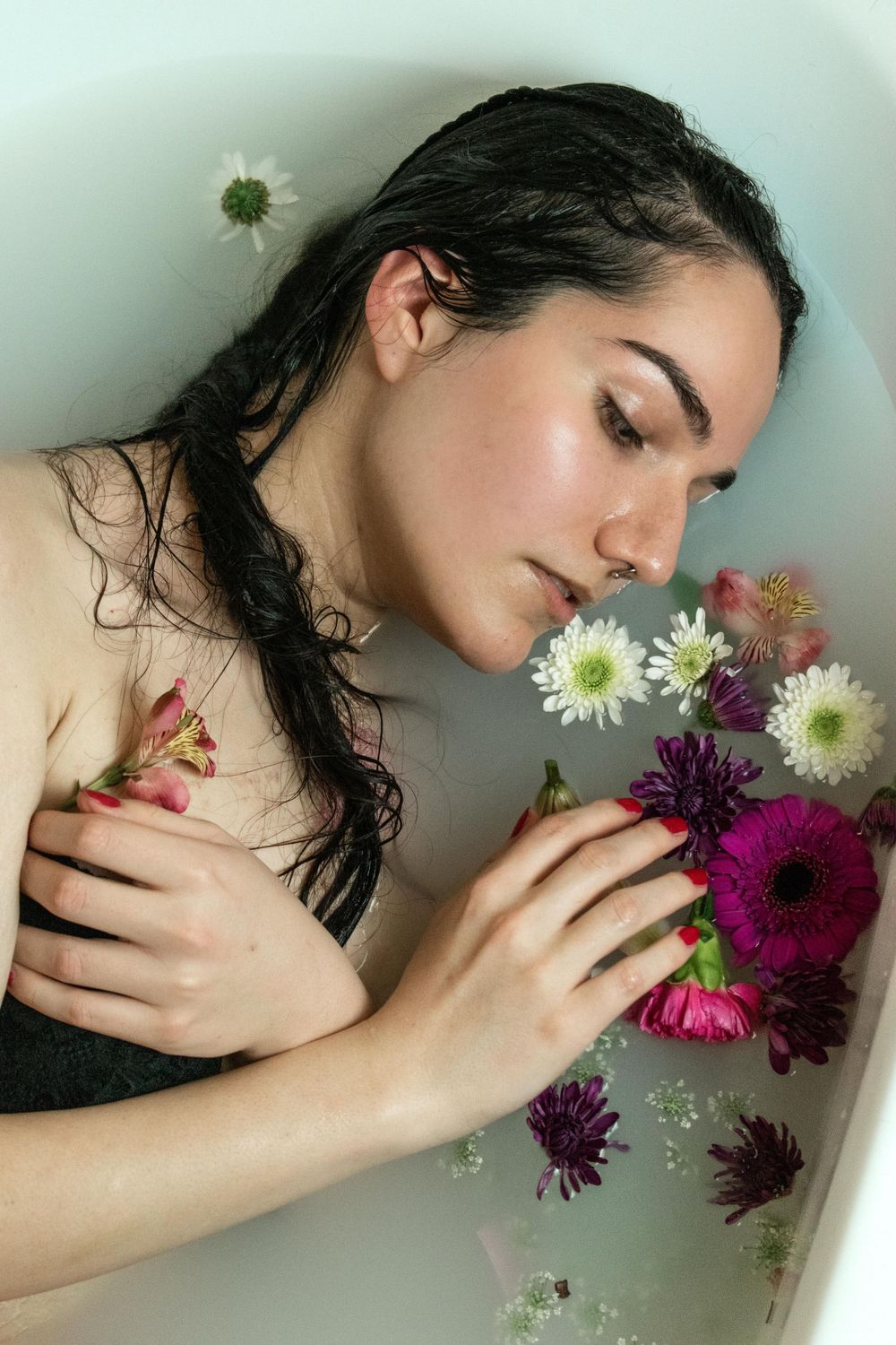 Ethereal portrait with floating flowers in milky bath water creating dreamy atmosphere.