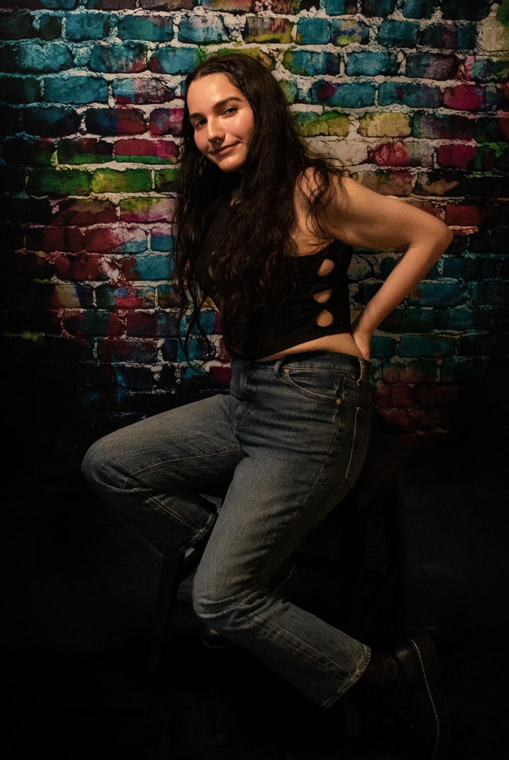 Fashion pose against vibrant graffiti wall wearing black top and denim.