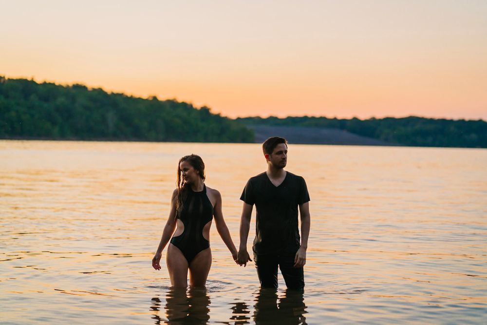 Couple holding hands while standing in tranquil lake water at dusk.