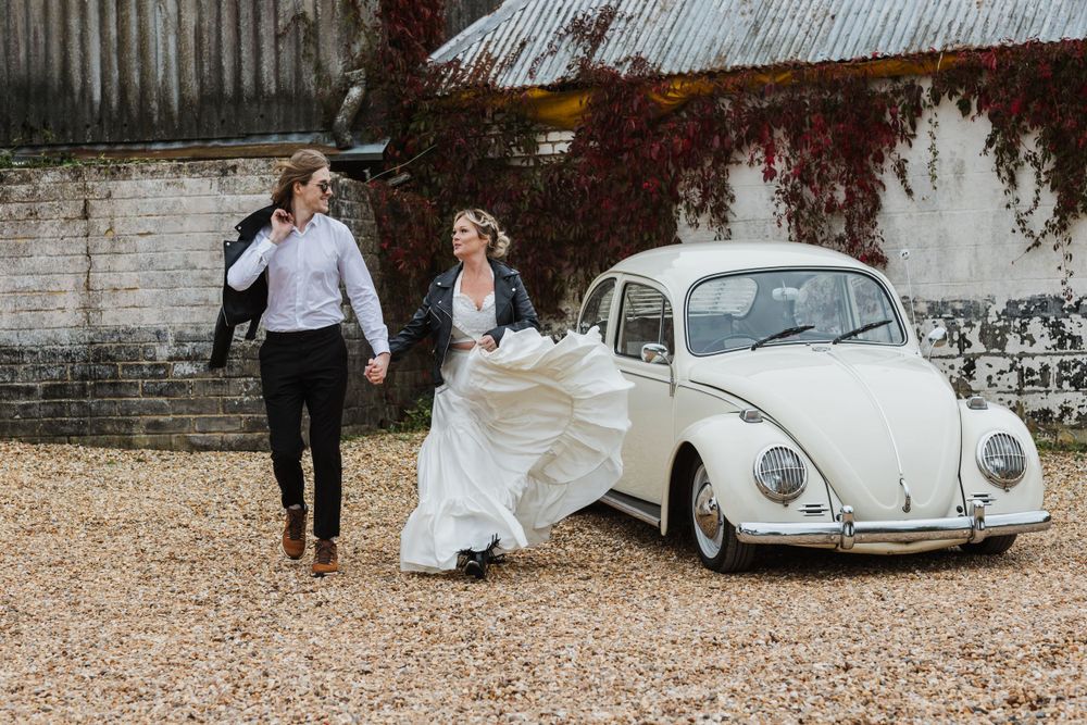 couple running by a Bug car wearing wedding attire and looking at each other