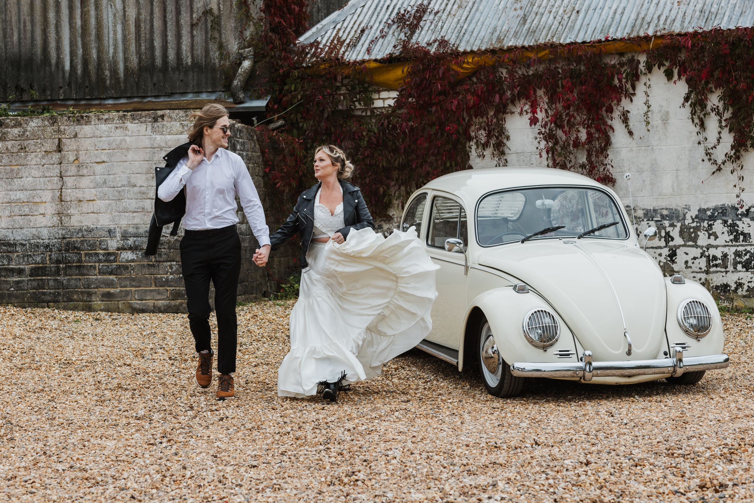 couple running by a Bug car wearing wedding attire and looking at each other