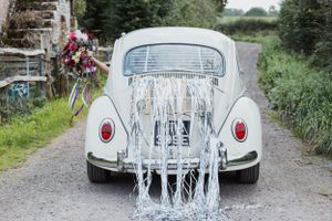 back view of a beetle bug car with tinsel hanging from the back with a hand holding flowers out the window