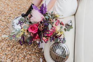 close up of beautiful bright bouquet of flowers with a bride sat on a white Beetle car with their foot on a mirrorball
