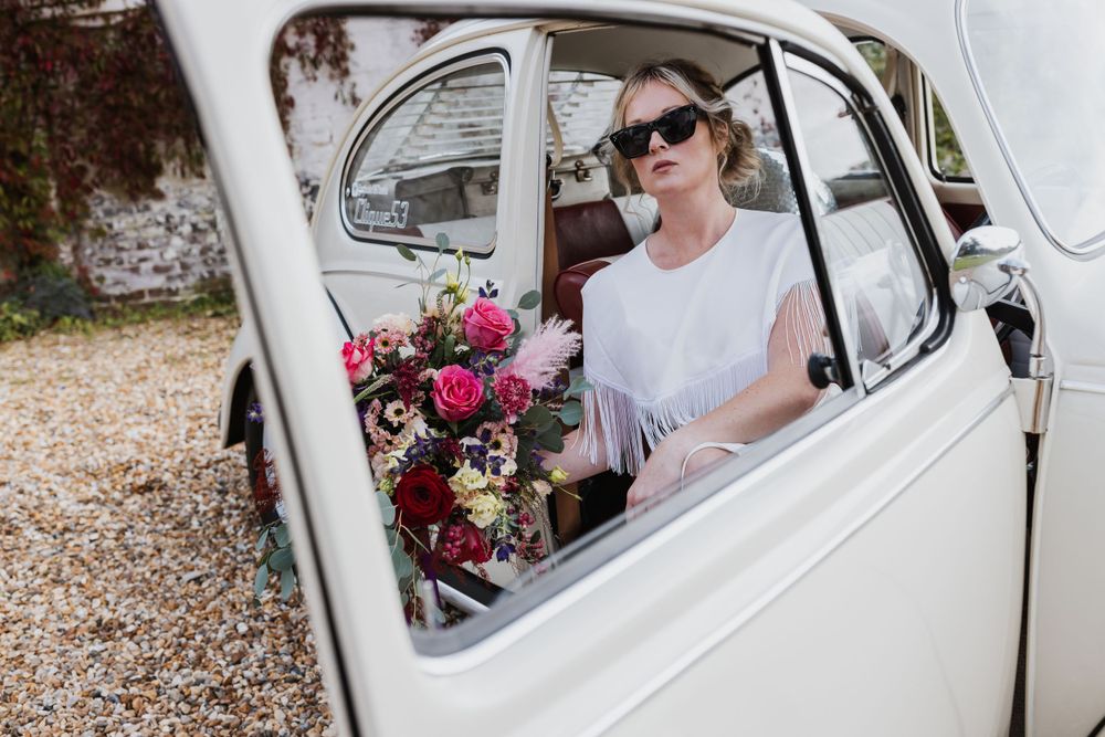 close up through the car window of female model with blonde hair in sunglasses holding a big bunch of colourful flowers.