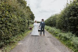 A couple in wedding dress and suit holding hands in front of Beetle bug car on a country path