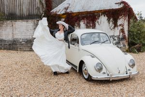 couple running by a Bug car wearing wedding attire and looking at each other