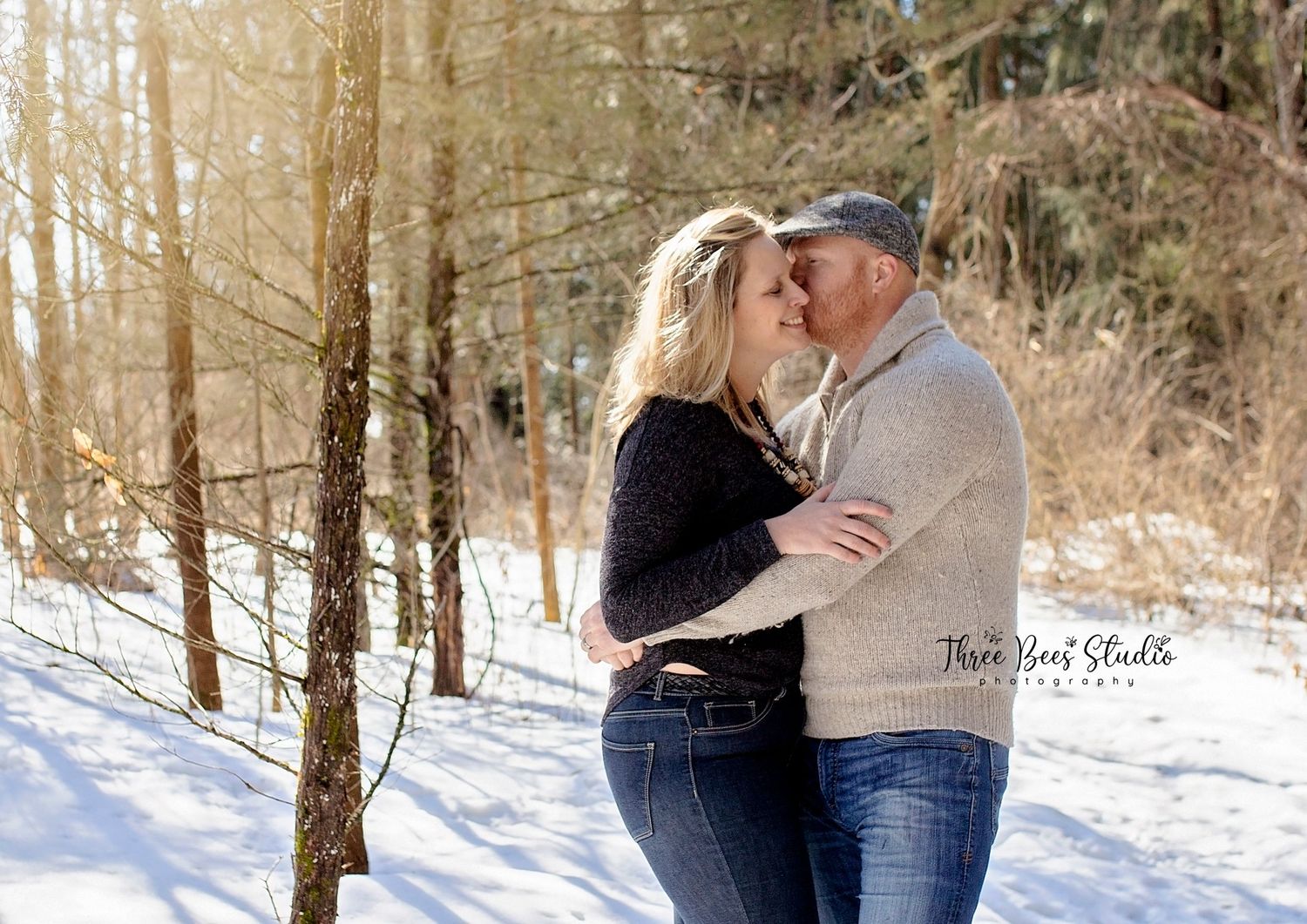 A romantic winter portrait of a couple embracing among snow-covered trees in a forest setting.