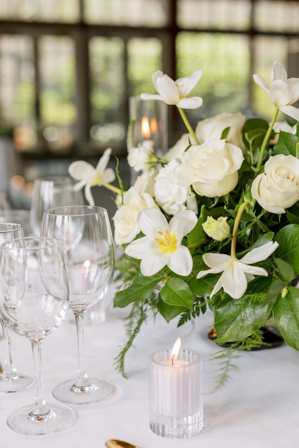 Elegant wedding reception table setting with white roses, candles, and crystal wine glasses.