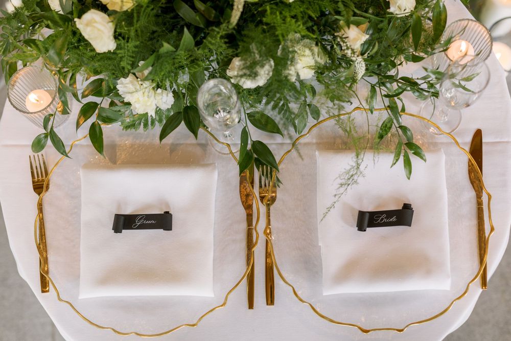 Overhead view of elegant place settings with gold flatware and lush white floral centerpiece.