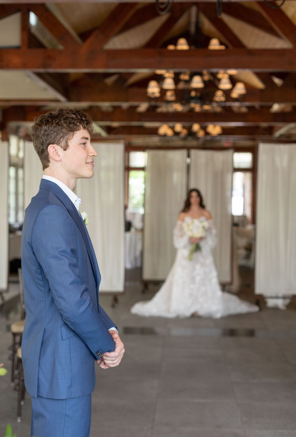 First look moment in a rustic venue with exposed wooden beams and natural lighting.