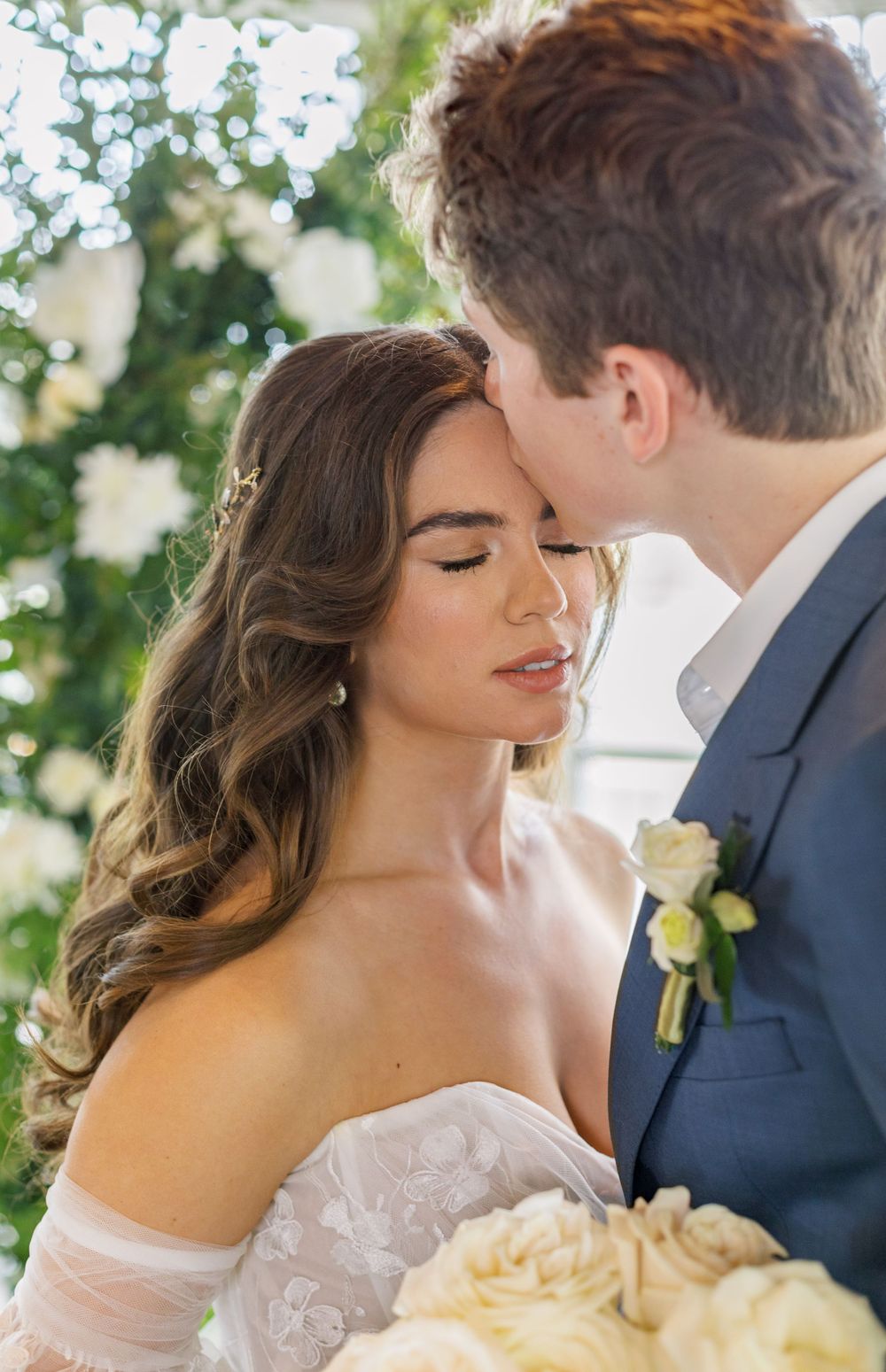 A tender wedding moment captured in soft lighting with white florals and a navy suit.