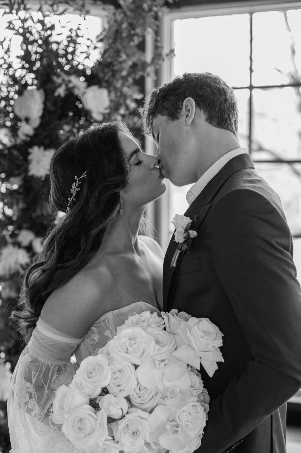 Romantic black and white photo of wedding couple sharing kiss with white roses.