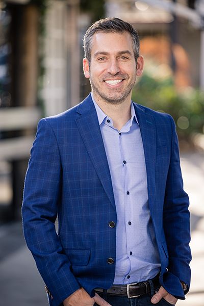 Man wearing light blue shirt and blue jacket smiling at camera