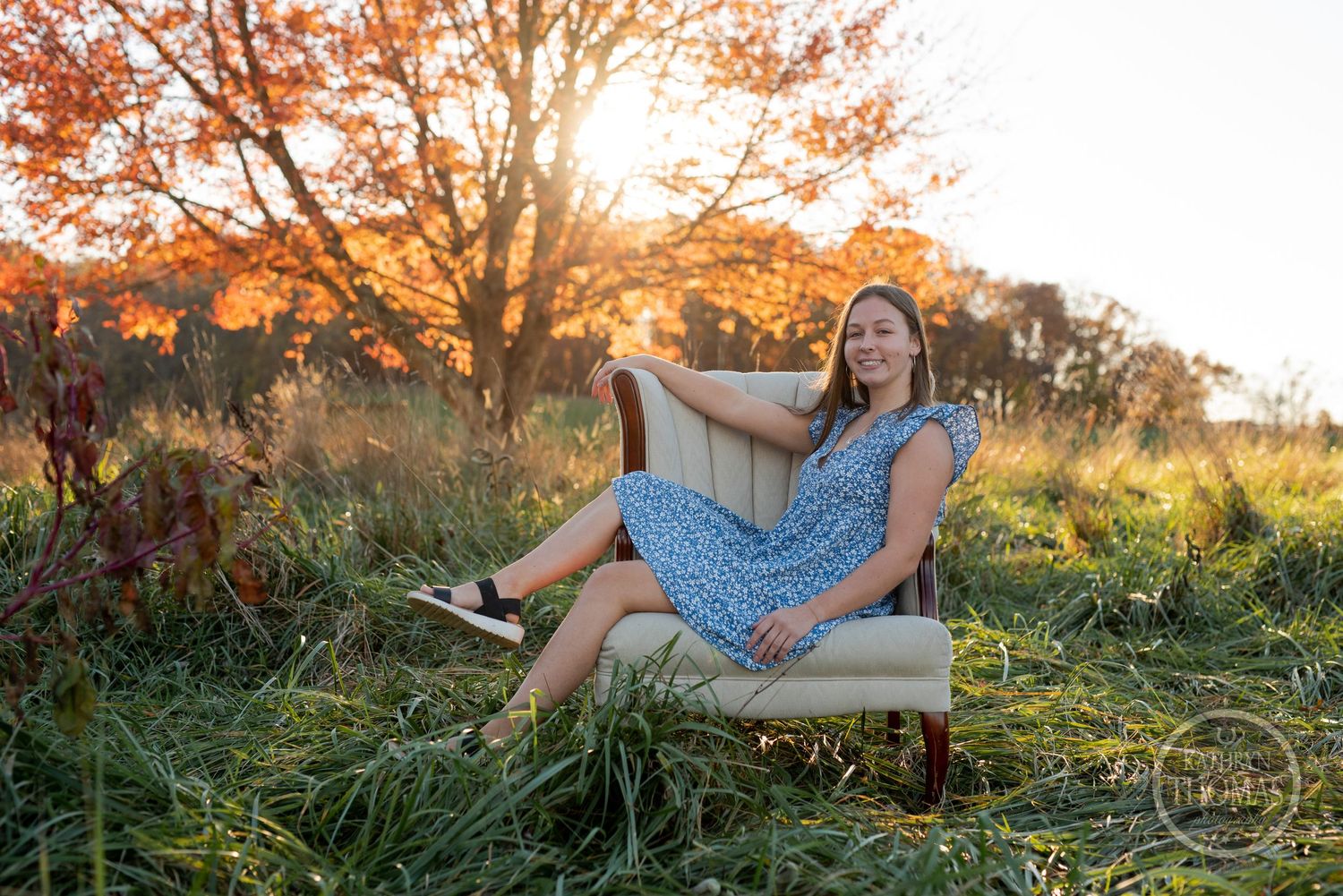 A blue floral dress on a vintage beige armchair in a sun-dappled autumn field.