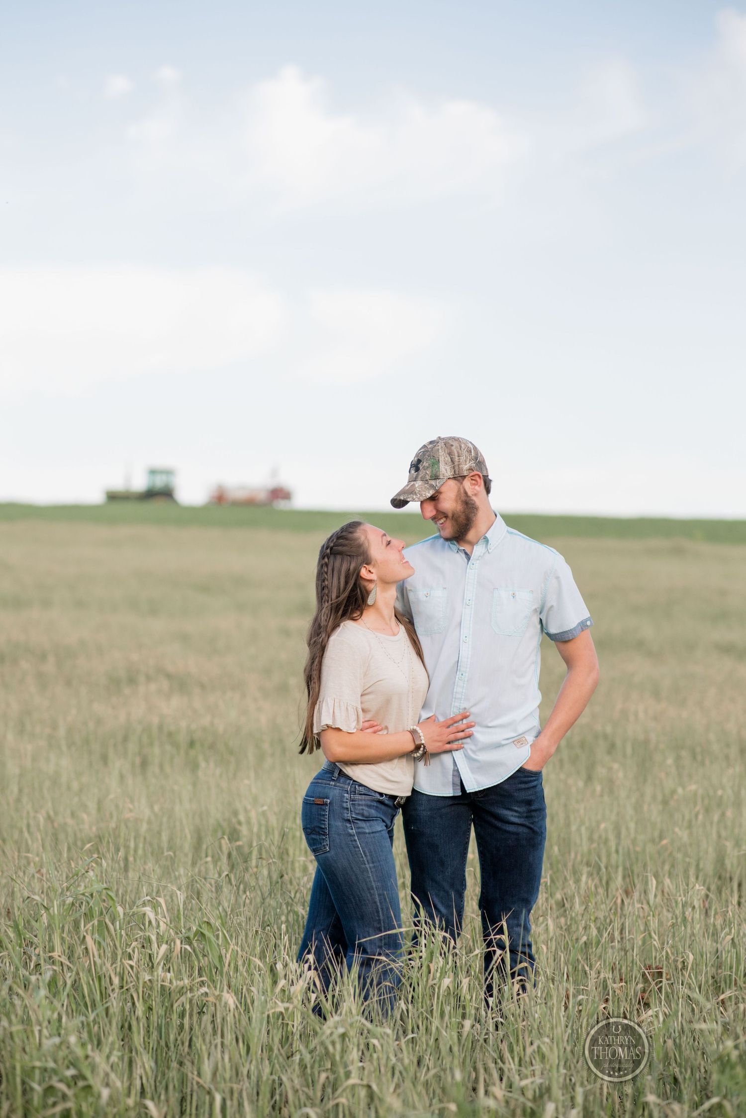 A couple embraces while standing in a serene grassy field on a sunny day.
