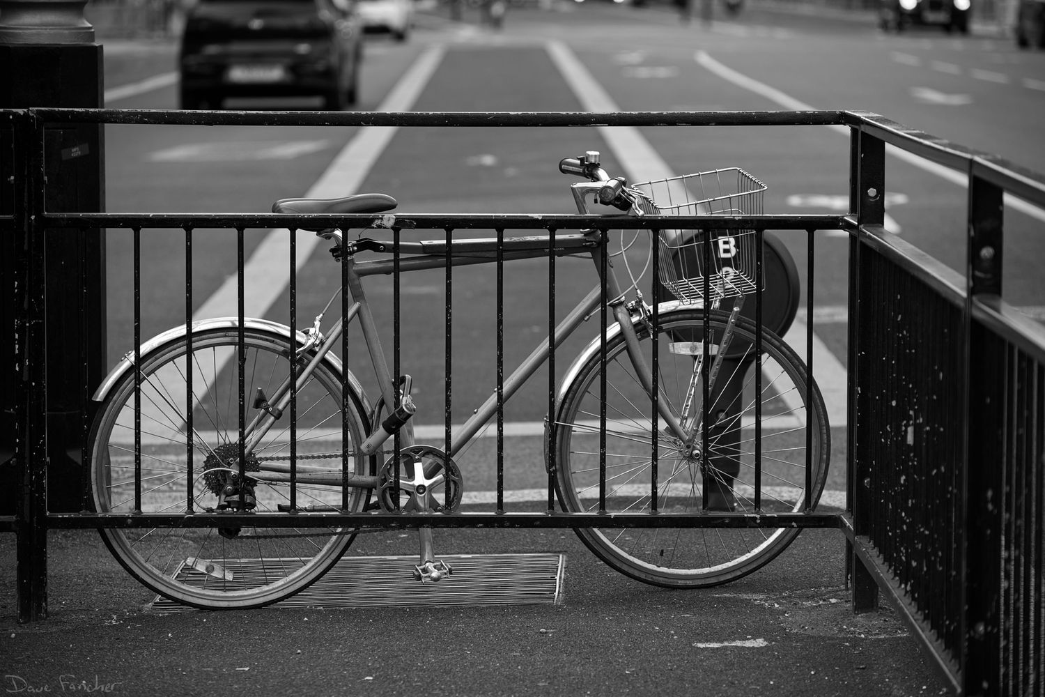 Black and white. A bike is locked to a crosswalk fence in London, England.