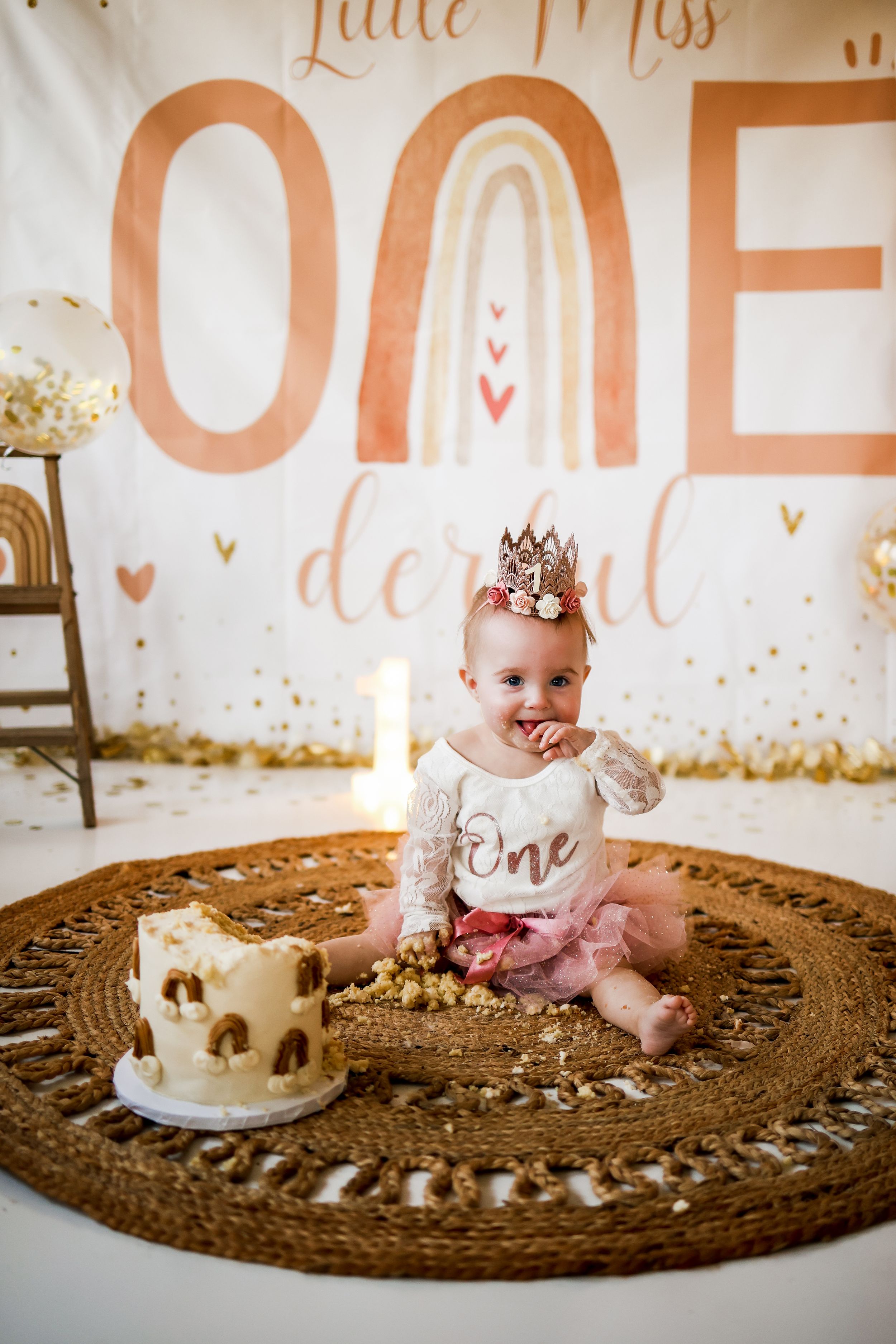 First birthday cake smash session with decorated cake and gold lettering backdrop.