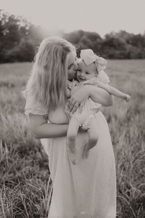 Black and white portrait of tender moment between mother and baby in field.