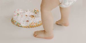 Close up view of tiny feet next to a white decorated birthday cake on a white platform.