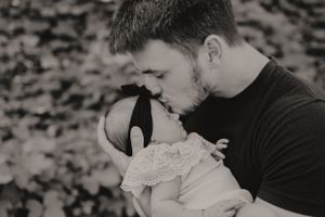Black and white intimate portrait of father kissing baby's head.