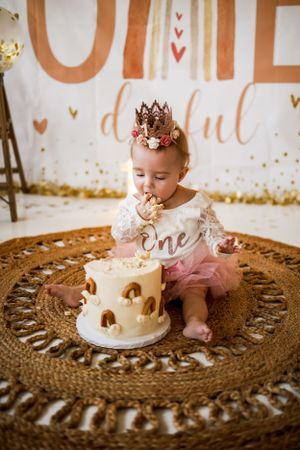 Baby in tutu and crown enjoying cake smash photoshoot on circular jute rug.
