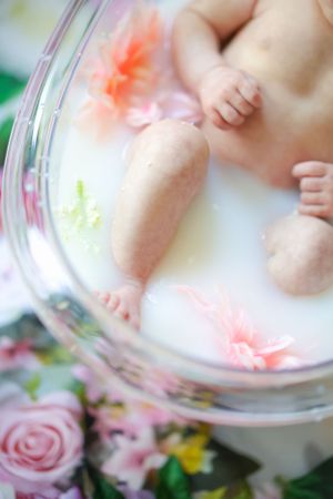 Baby feet reflected in a mirror surrounded by delicate pink flowers and soft lighting.